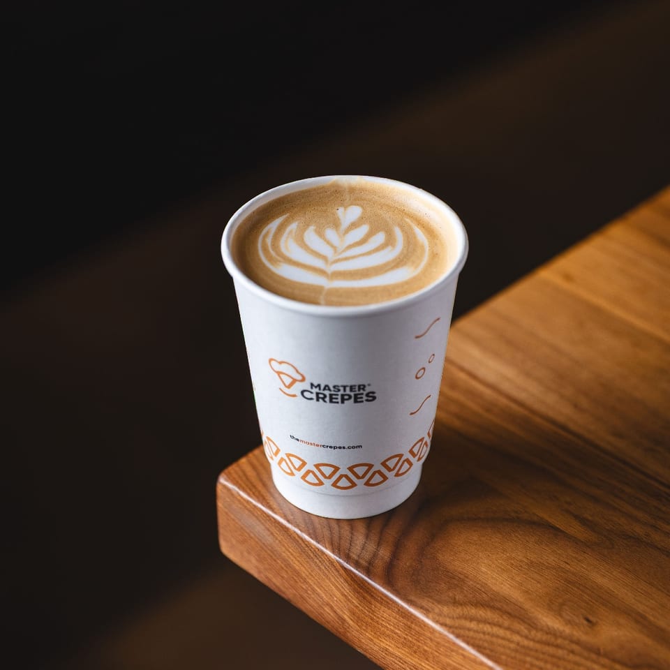 Latte with leaf-shaped foam art in a Master Crepes cup