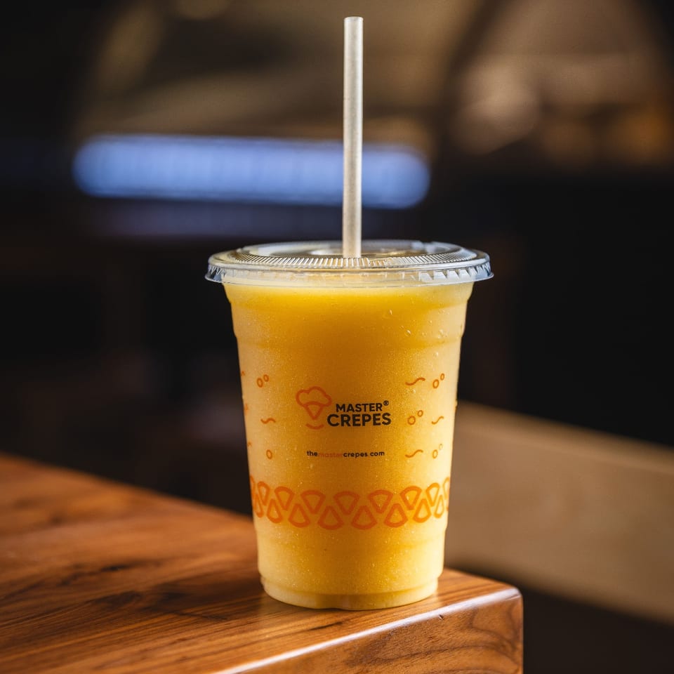 Yellow frozen drink in a Master Crepes cup on a wooden table