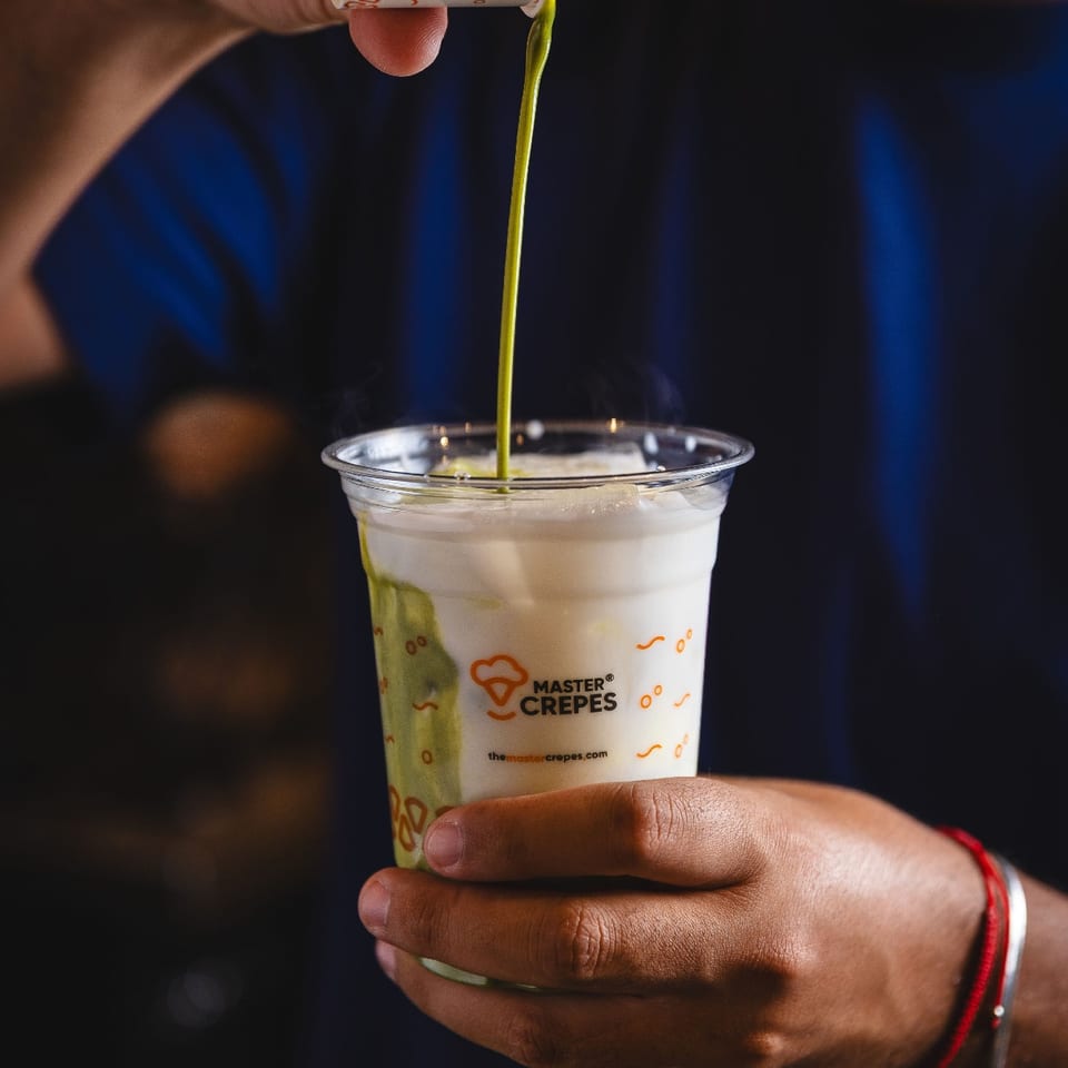 Green tea being poured into milk in a Master Crepes cup